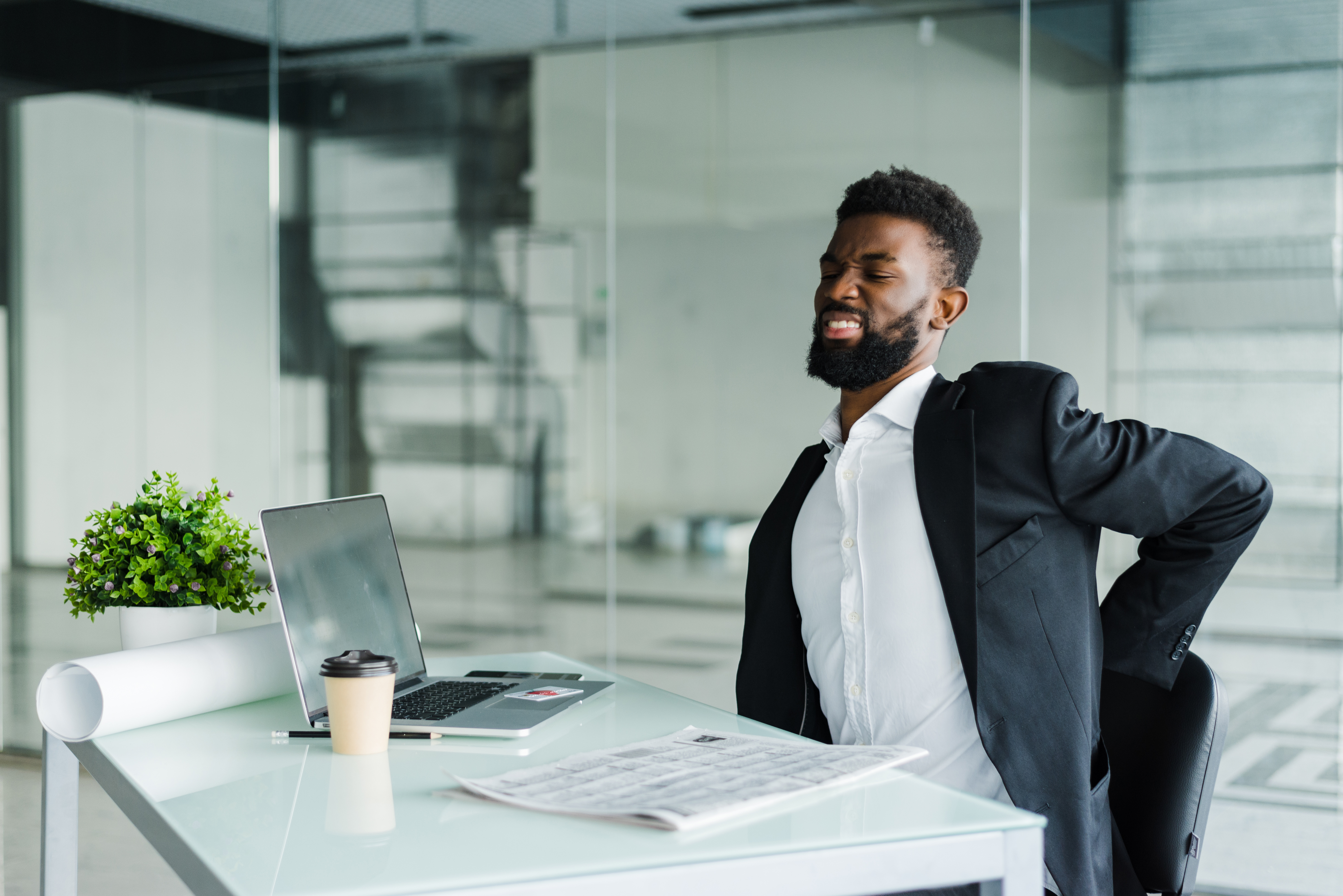 Young businessman in office at desk suffering from back pain in office Young Businessman In Office At Desk Suffering From Back Pain